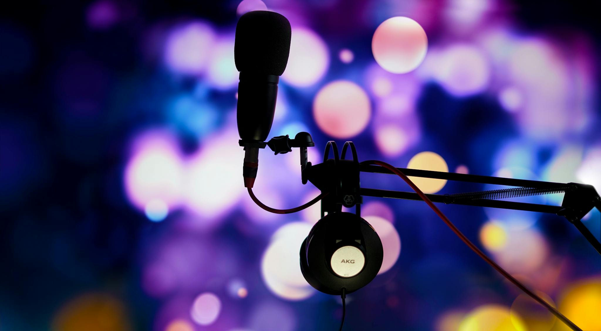 A studio microphone and headphones in silhouette against a vibrant bokeh background.
